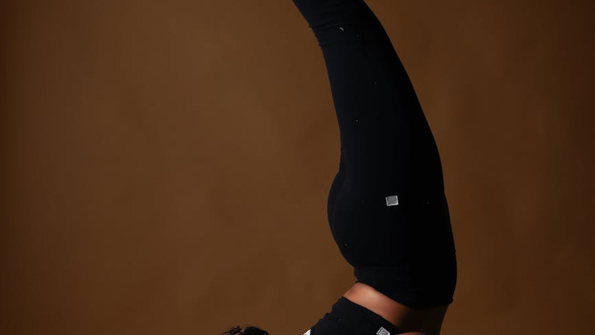 Person in a calm, controlled yoga pose in a minimalist dark studio.